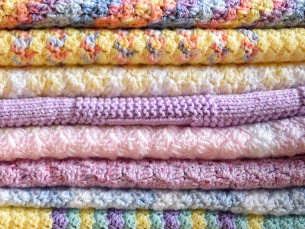 A pile of colourful folded knitted and crocheted blankets
